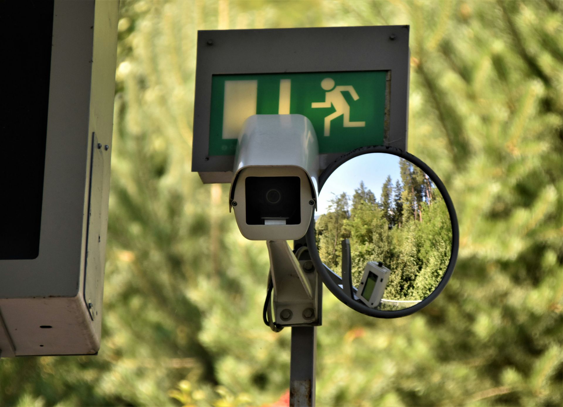A security camera is sitting next to a green exit sign.