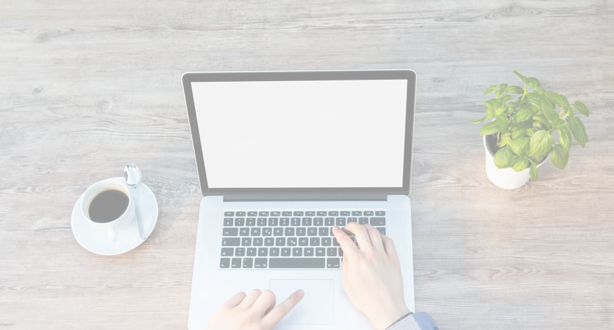 A person is typing on a laptop computer on a wooden table.