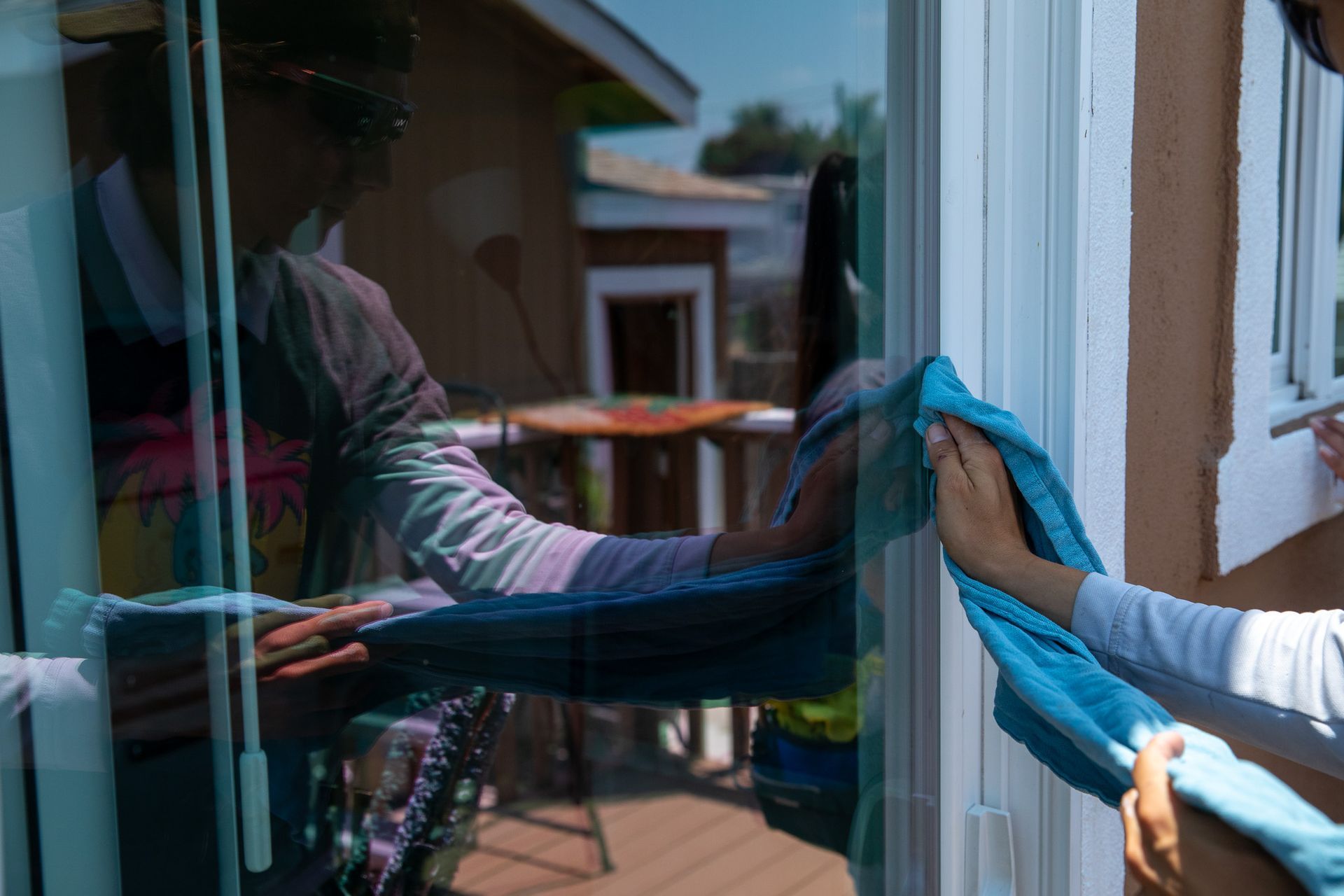 A woman is cleaning a sliding glass door with a blue cloth.
