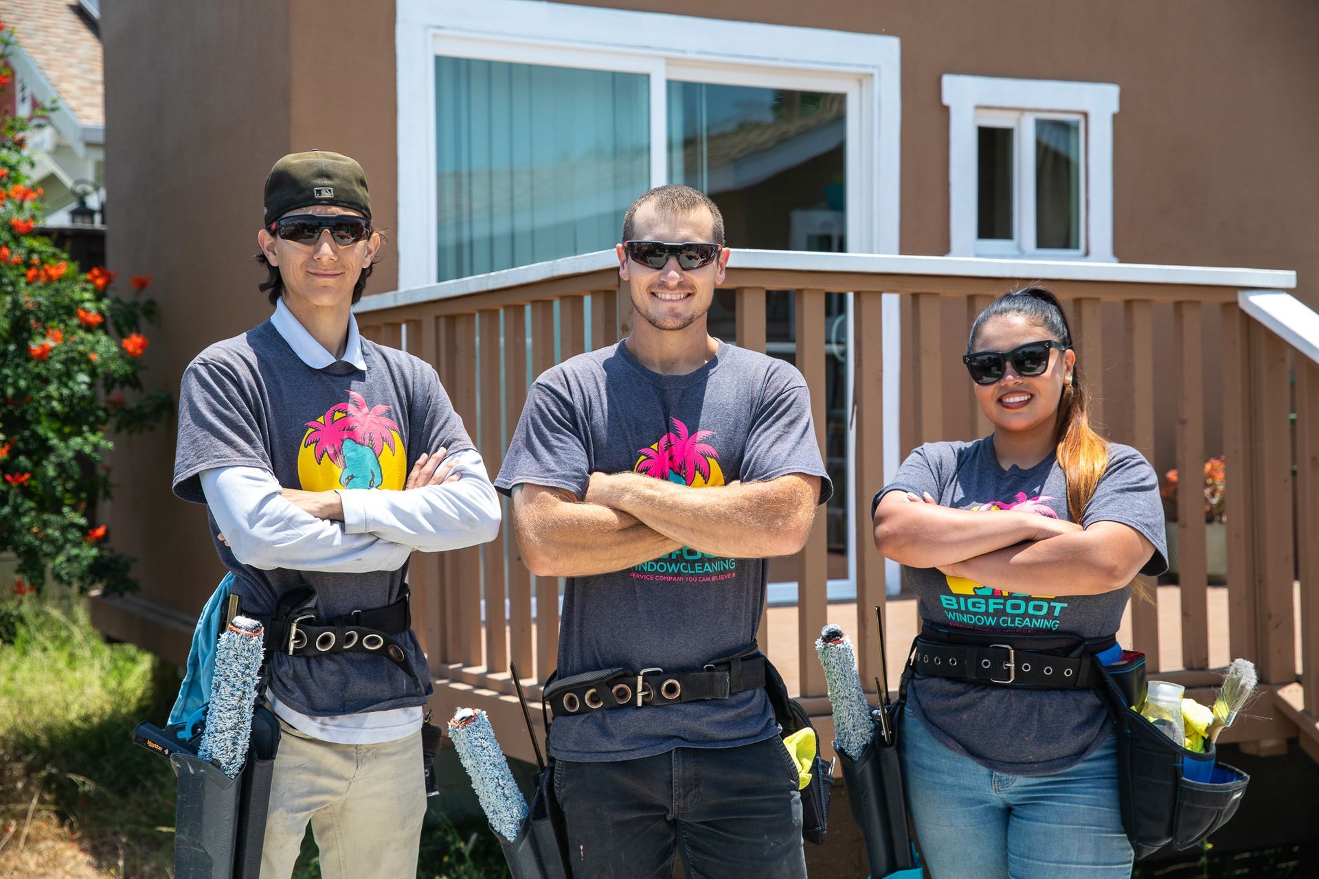 Three people are standing in front of a house with their arms crossed.
