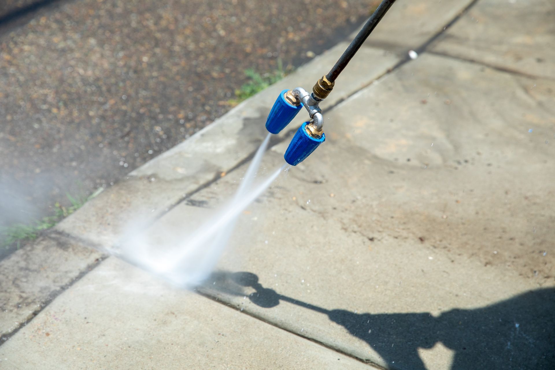 A person is using a high pressure washer to clean a sidewalk.