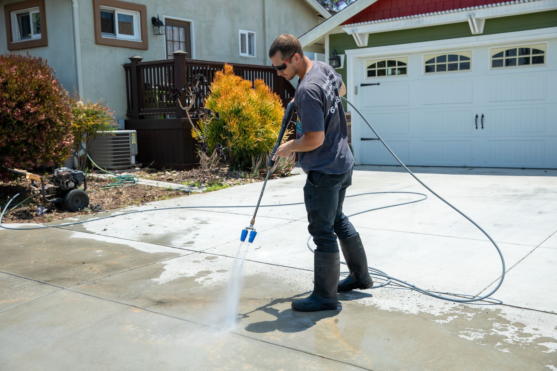 A man is using a high pressure washer to clean a driveway.