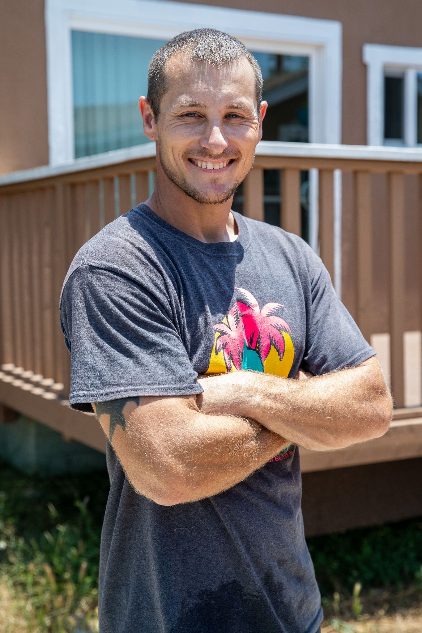 A man is standing in front of a house with his arms crossed and smiling.