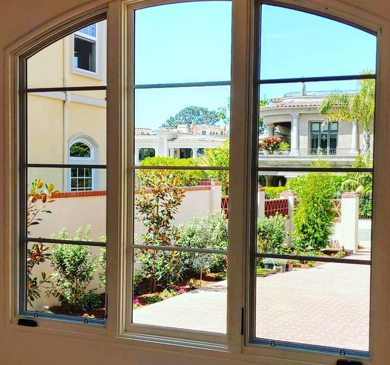 A window with a view of sunny houses, greenery, and a blue sky.