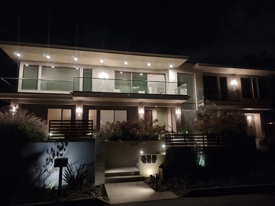 Two-story modern house at night, illuminated, with windows and a small yard.
