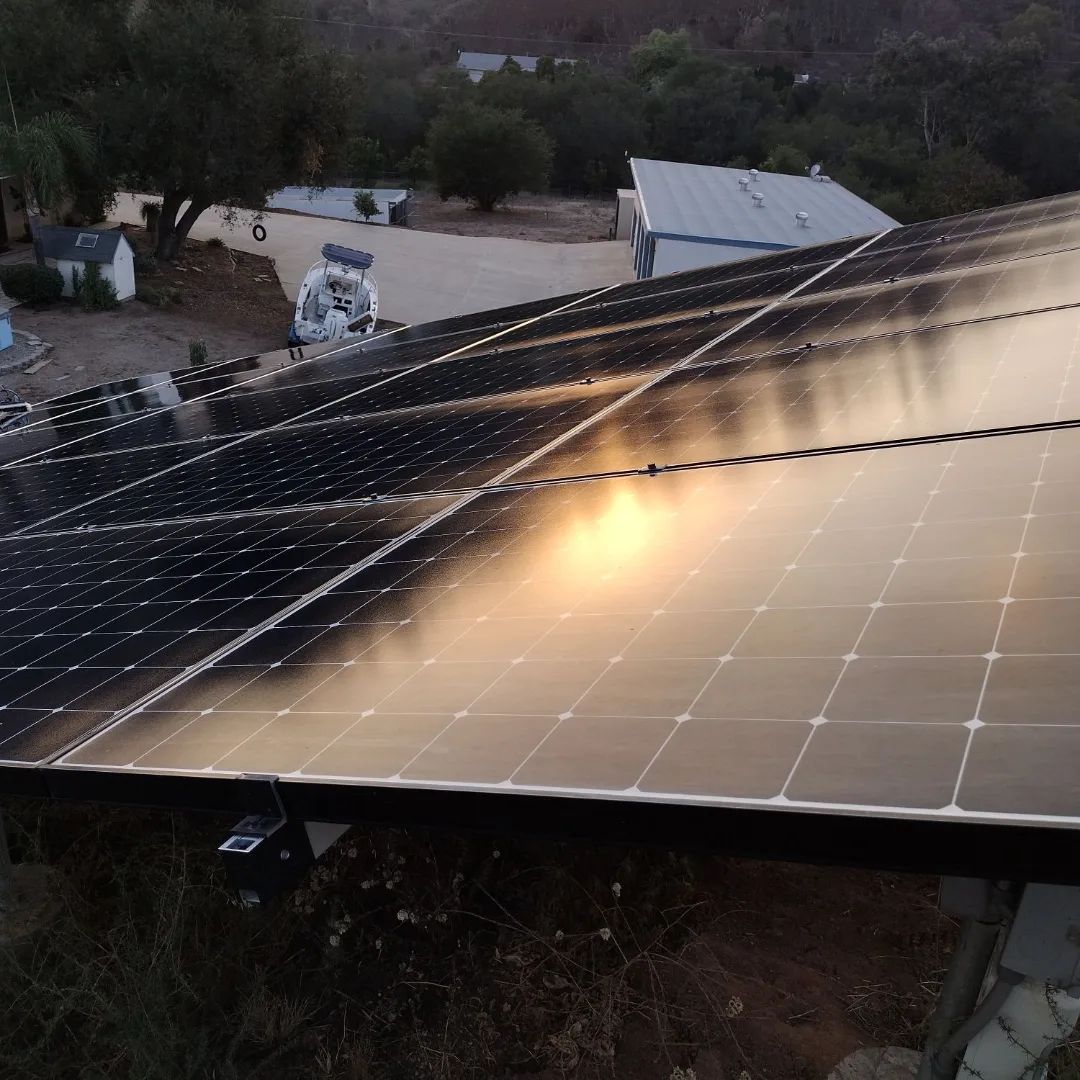Solar panels on a rooftop reflecting the sunset over a rural landscape.