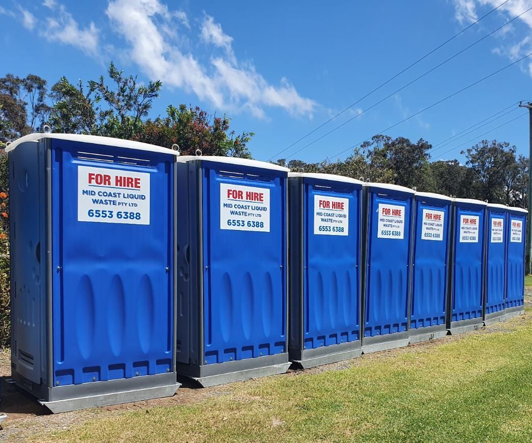 A Row of Blue Portable Toilets Are Lined Up in a Grassy Field — Mid Coast Liquid Waste In Rainbow Flat, NSW