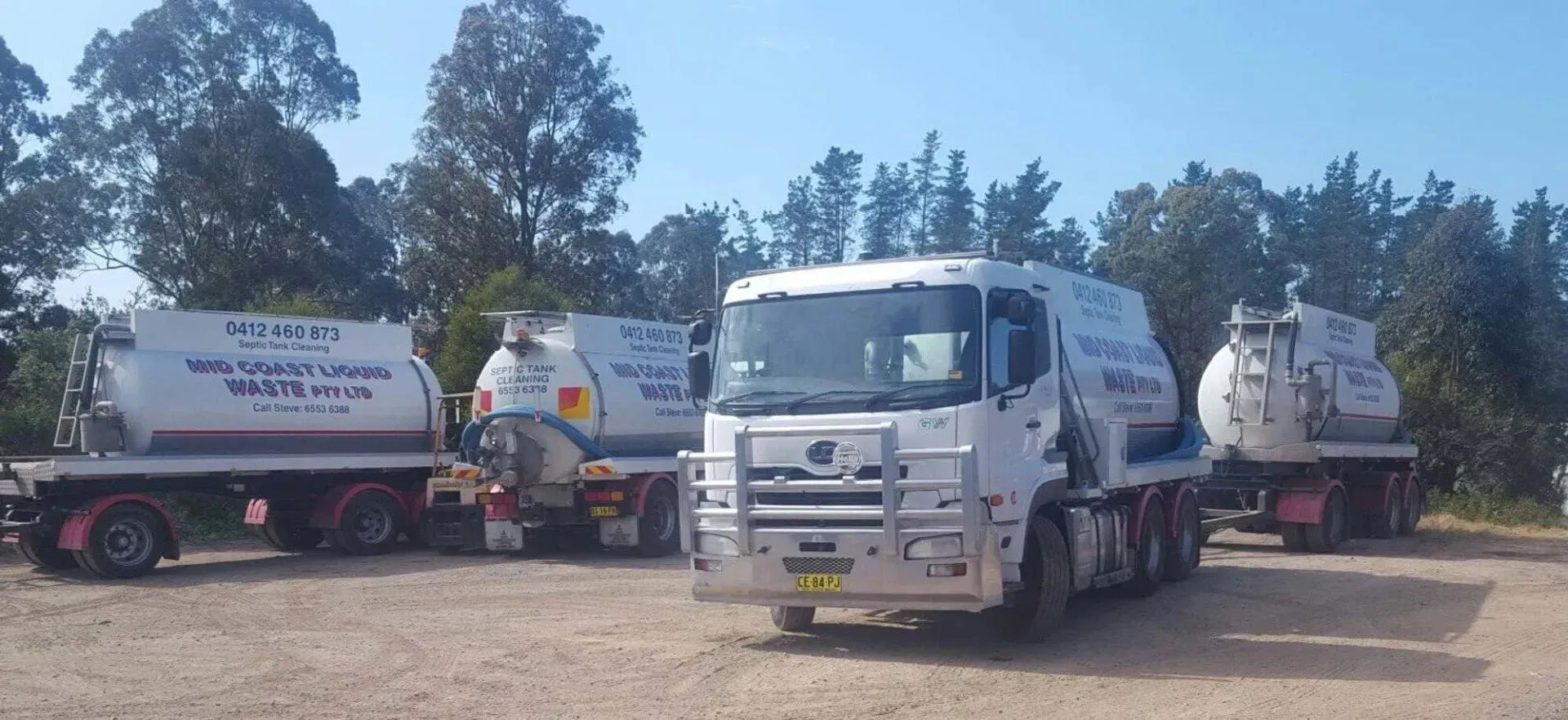 Three White Trucks Are Parked in a Dirt Lot With Trees in the Background — Mid Coast Liquid Waste In Bulahdelah, NSW