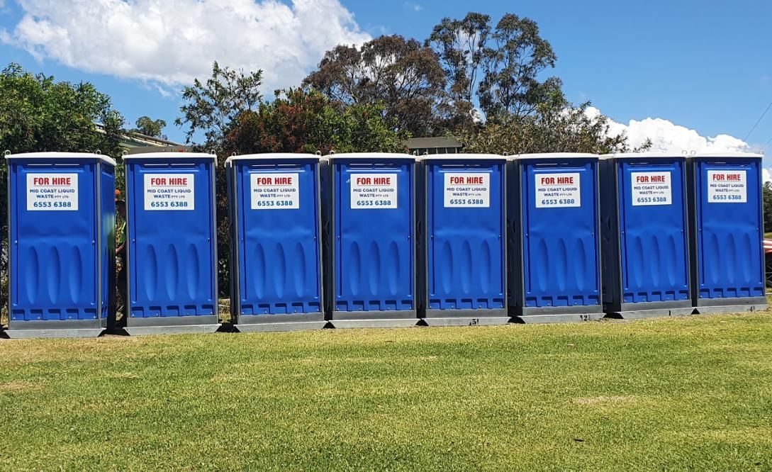 A Row of Blue Portable Toilets Are Lined Up in a Grassy Field — Mid Coast Liquid Waste In Rainbow Flat, NSW