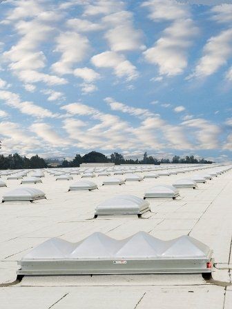 White roof with many skylights under a blue sky with scattered clouds.