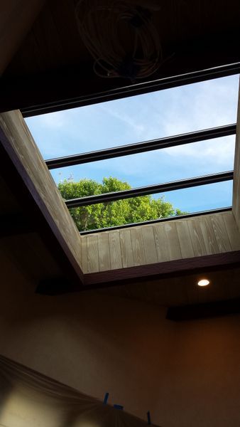 Skylight in a wooden ceiling looking at blue sky and green tree tops.