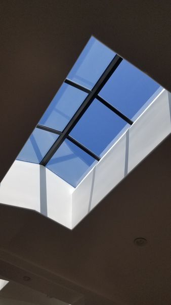 Skylight in a white ceiling, framed by black bars, against a blue sky.