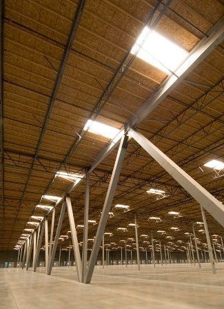 Interior view of a large warehouse with metal support beams and skylights in the ceiling.