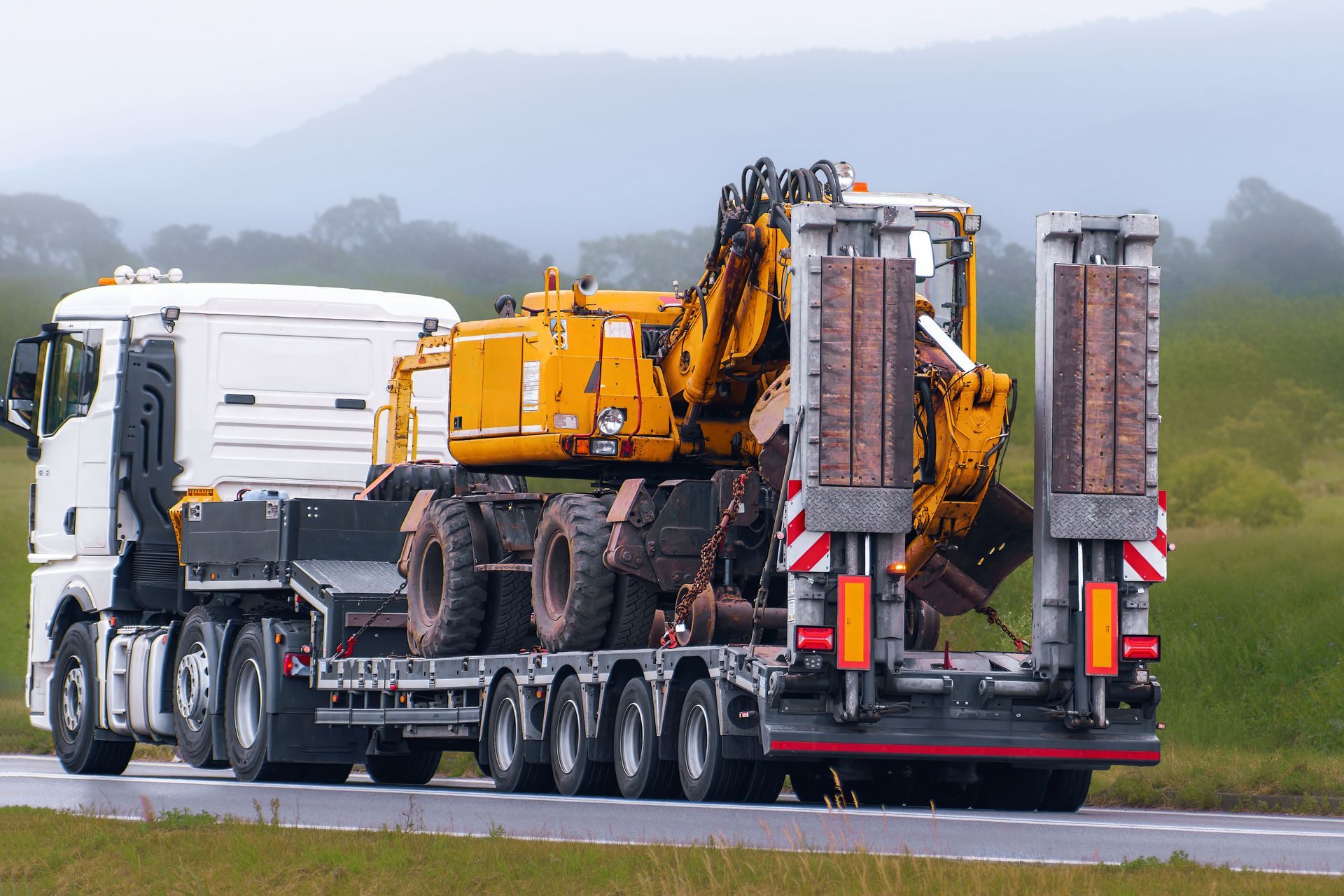 Flatbed truck transporting heavy construction equipment along a highway.