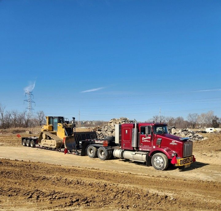 Truck hauling large yellow machinery off-road under a blue sky.
