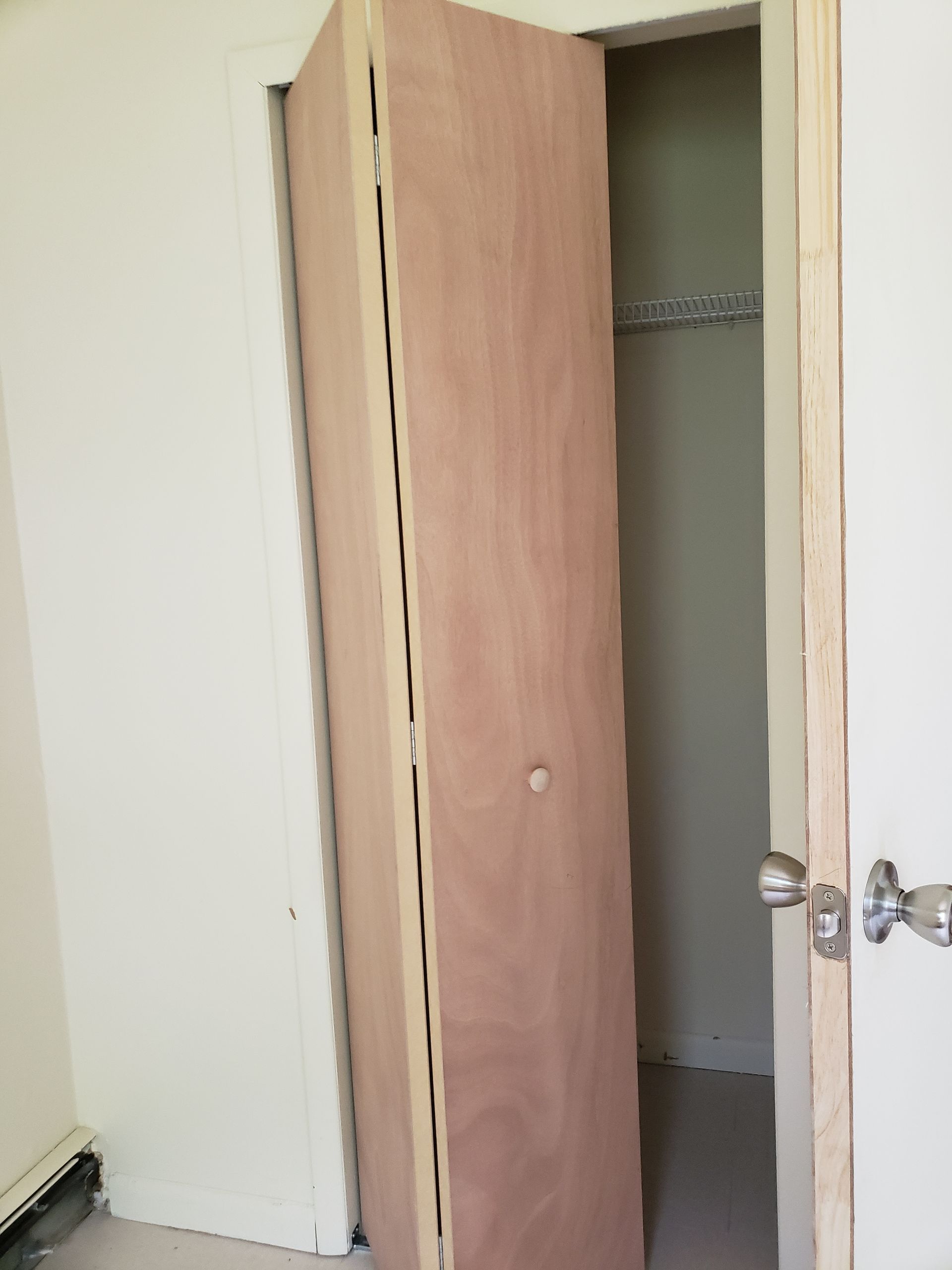 A wooden door is open to a closet in a room.