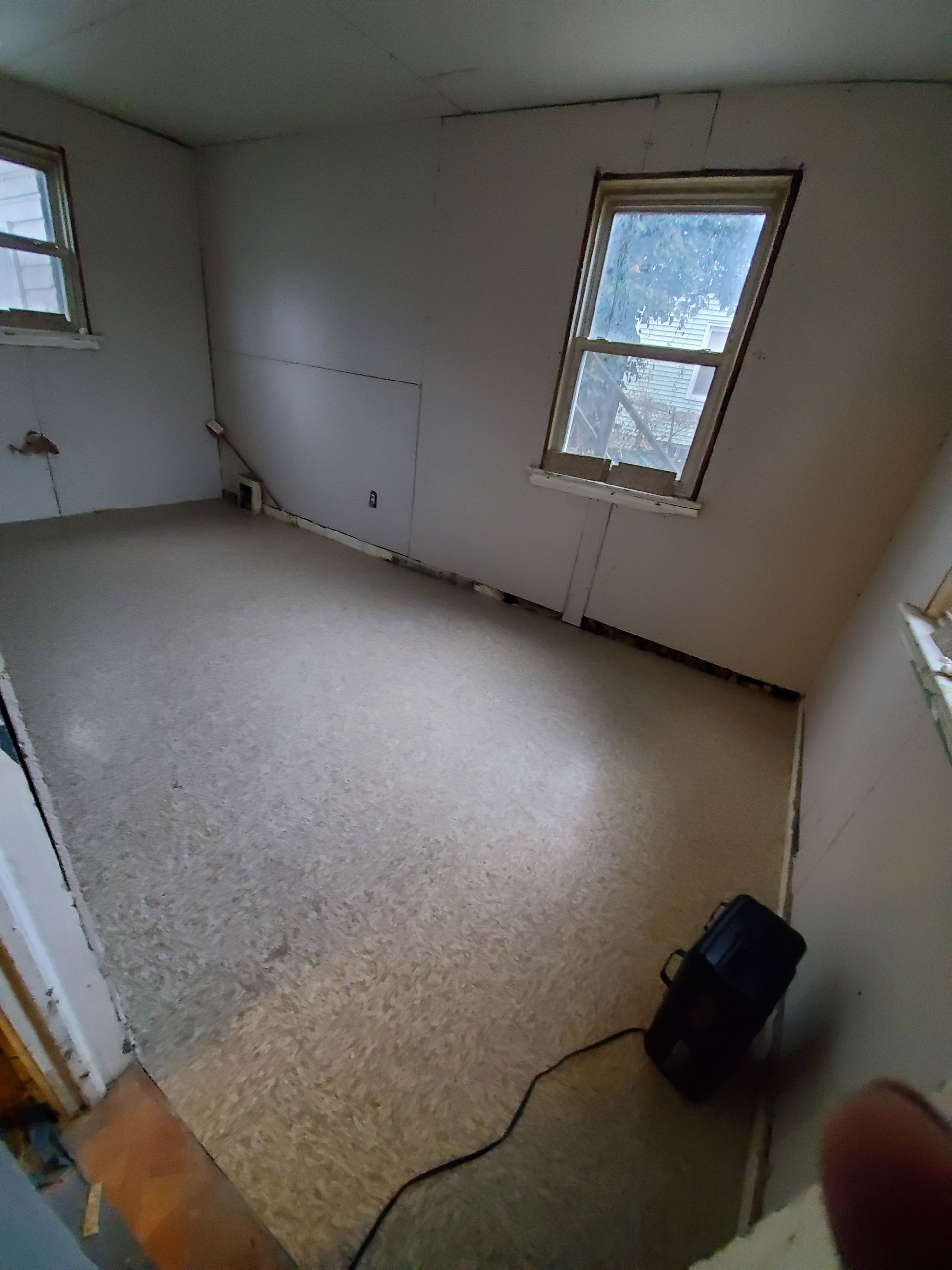 An empty room with two windows and a vacuum cleaner