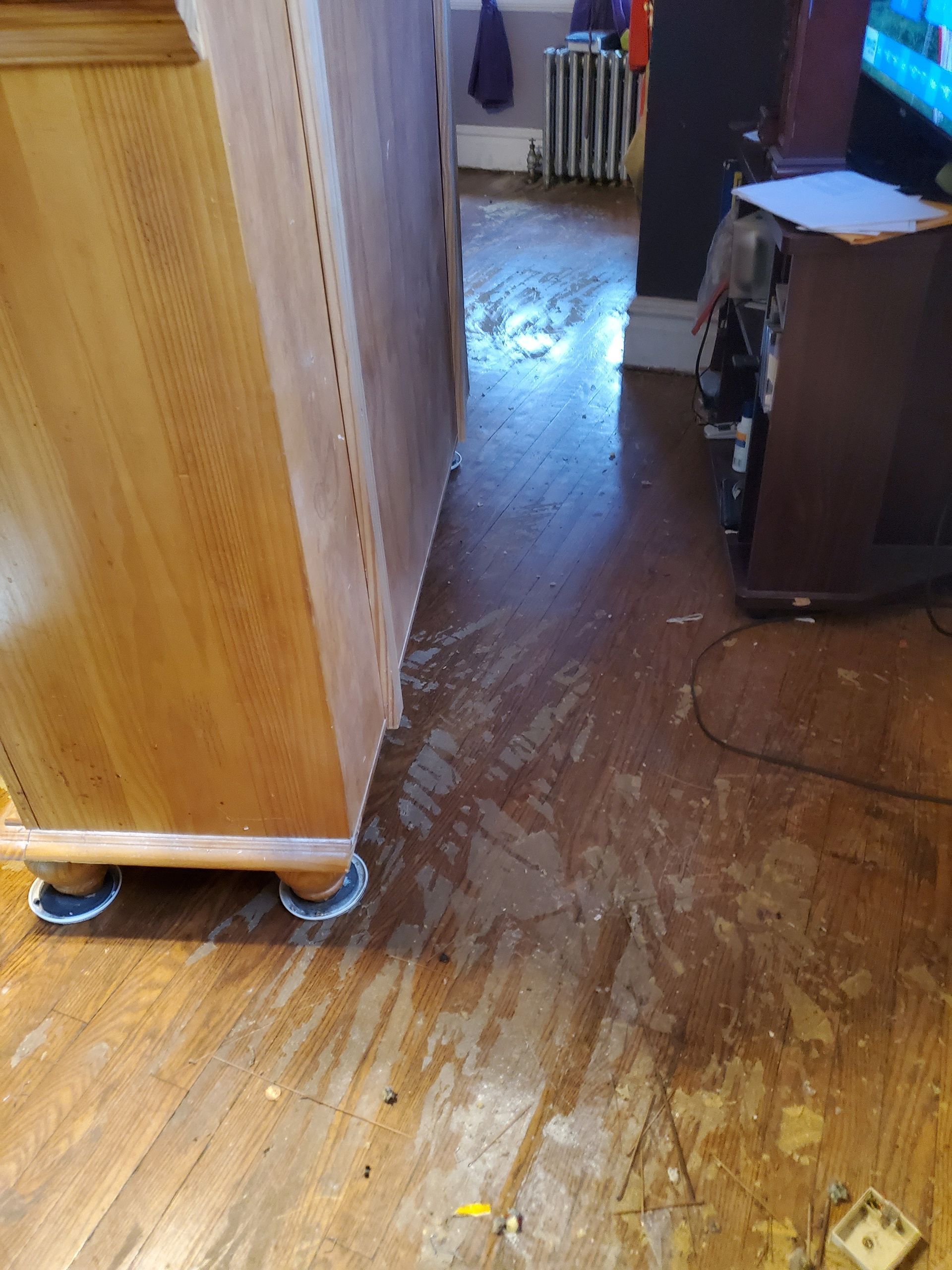 A dirty wooden floor in a room with a dresser and a television.
