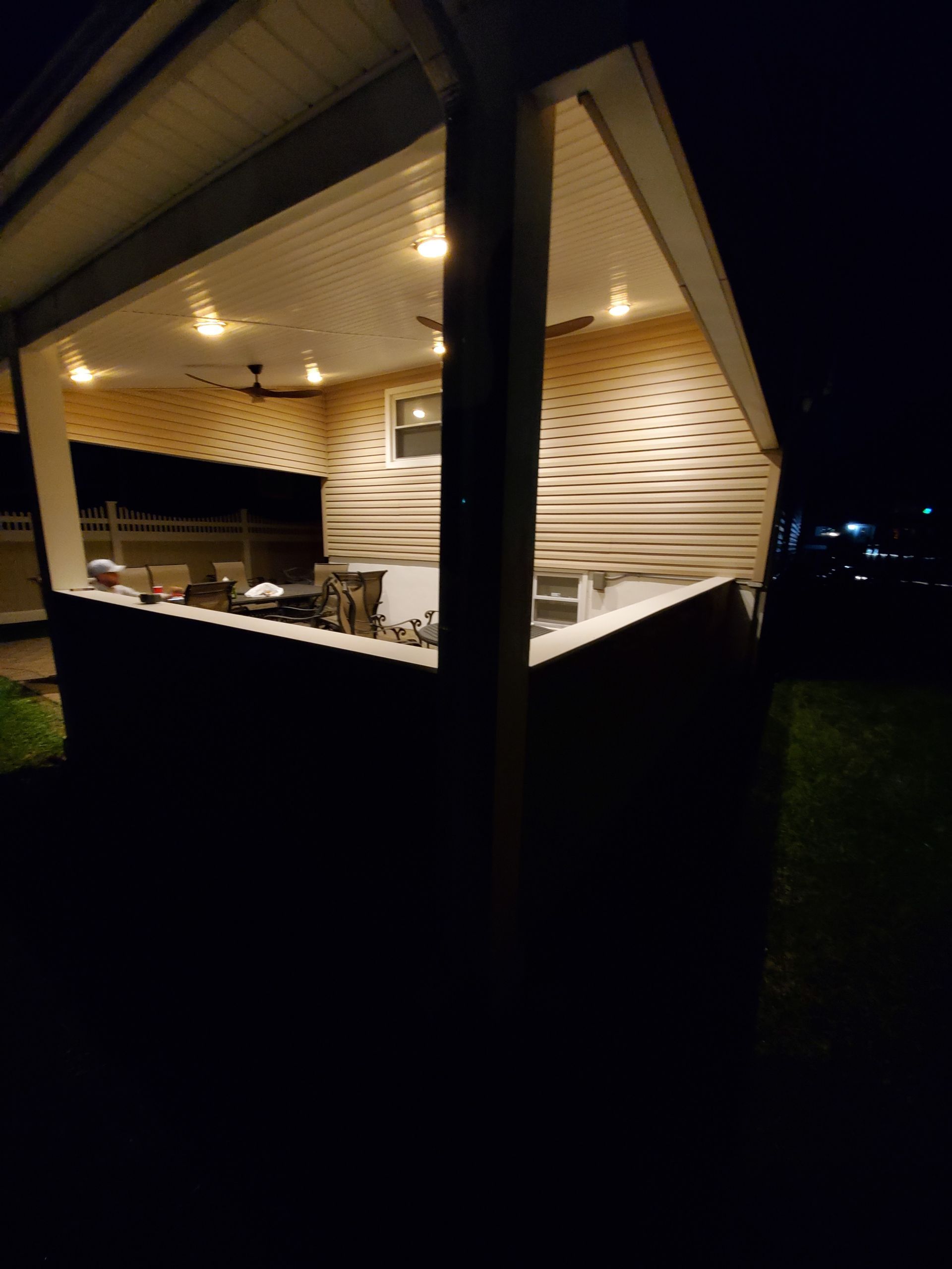 A covered patio with a ceiling fan and lights at night.