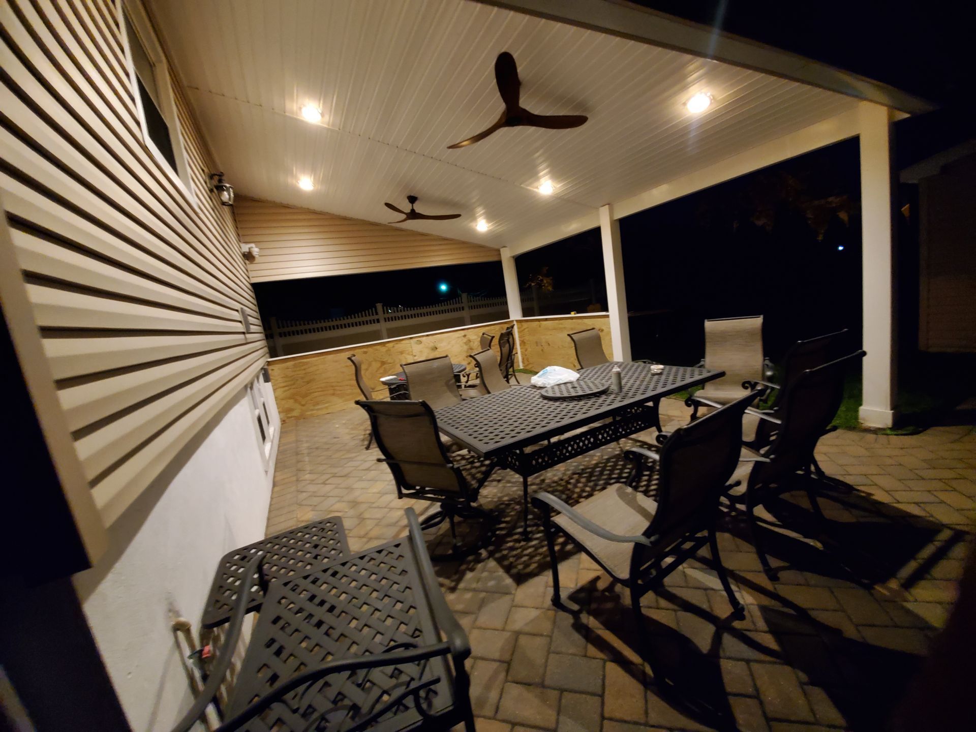 A patio with a table and chairs and a ceiling fan at night.