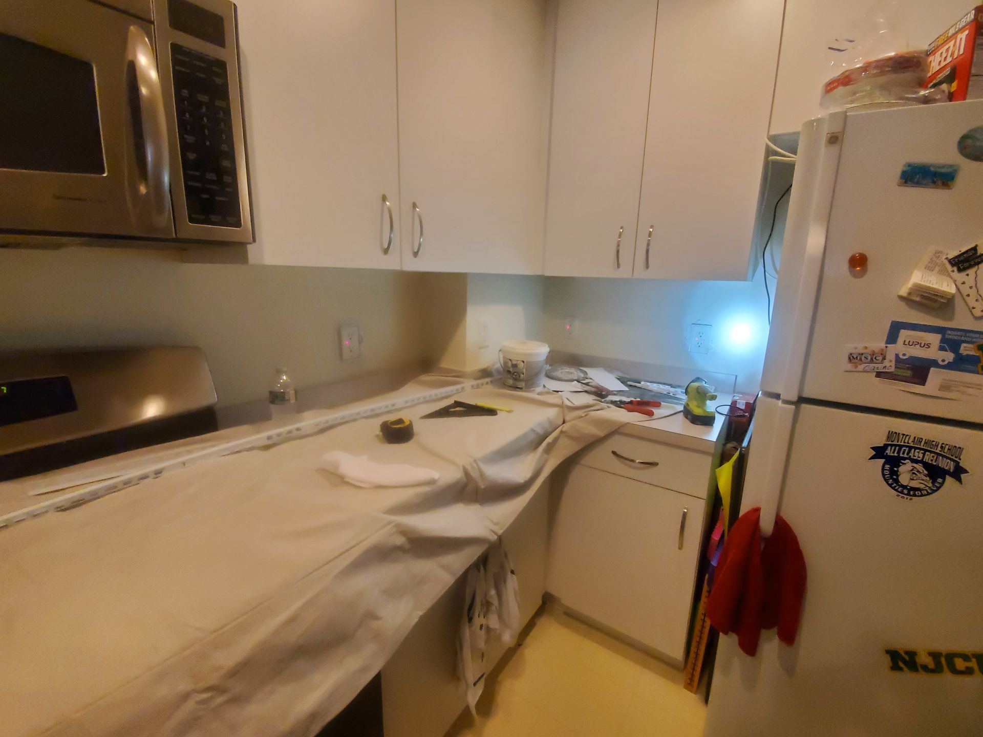 A kitchen with white cabinets , a refrigerator and a microwave.