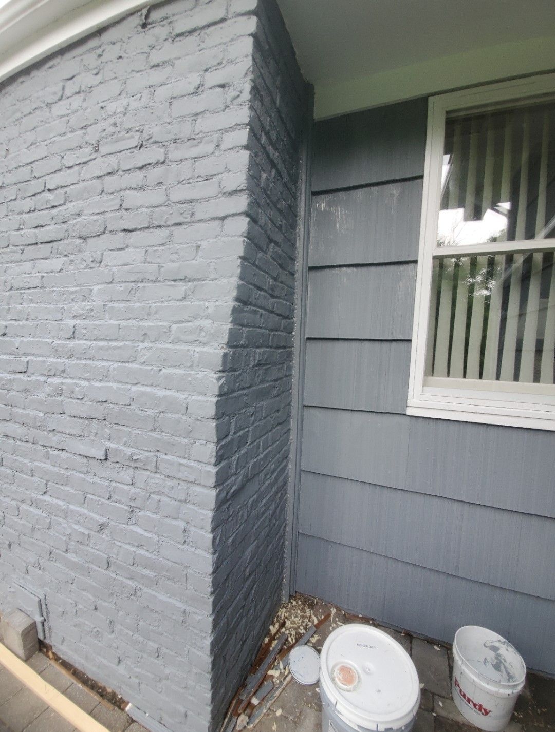A corner of a house with buckets of paint on the ground.