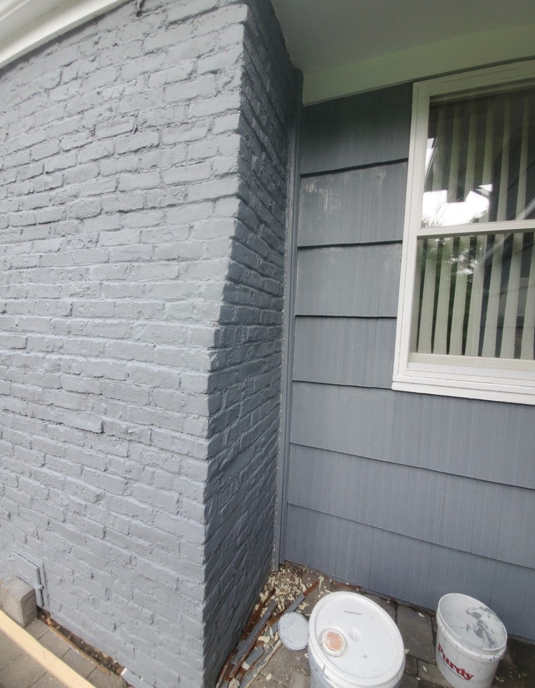 A gray brick wall with a window and buckets of paint on the ground.