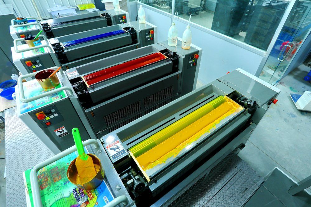 Ink printing machines with yellow, red, blue, and black inks, in a factory setting.