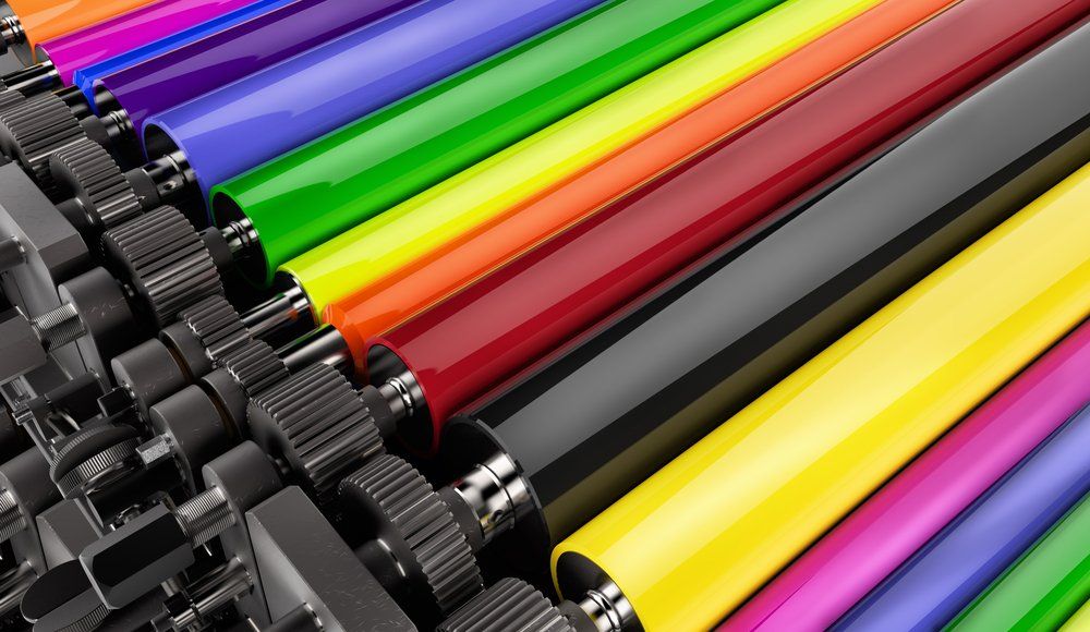 Ink rollers in a printing press, various colors: purple, blue, green, yellow, red, black. Gears are visible.
