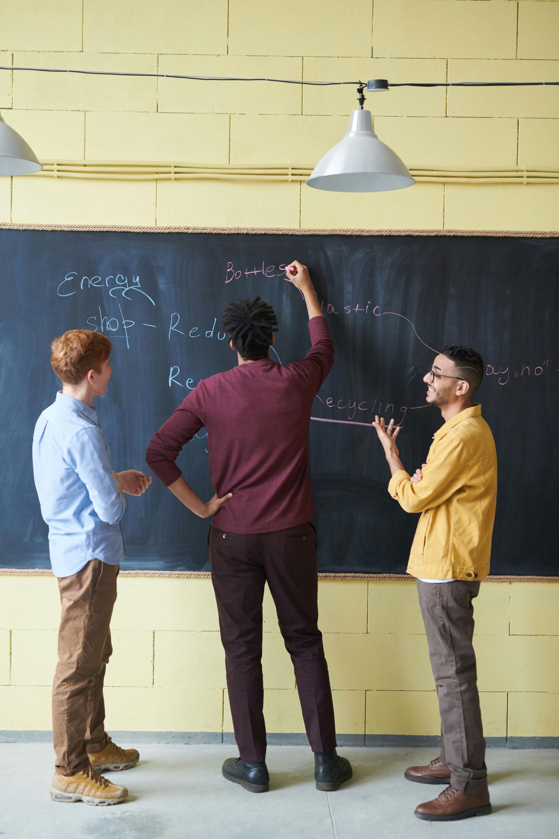 Three men are standing in front of a blackboard writing on it.