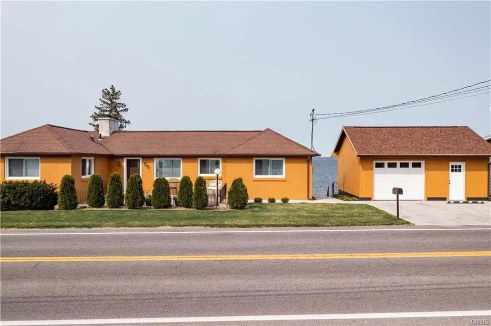 Orange-colored house and garage with brown roof, green grass, and road in front against a light blue sky.