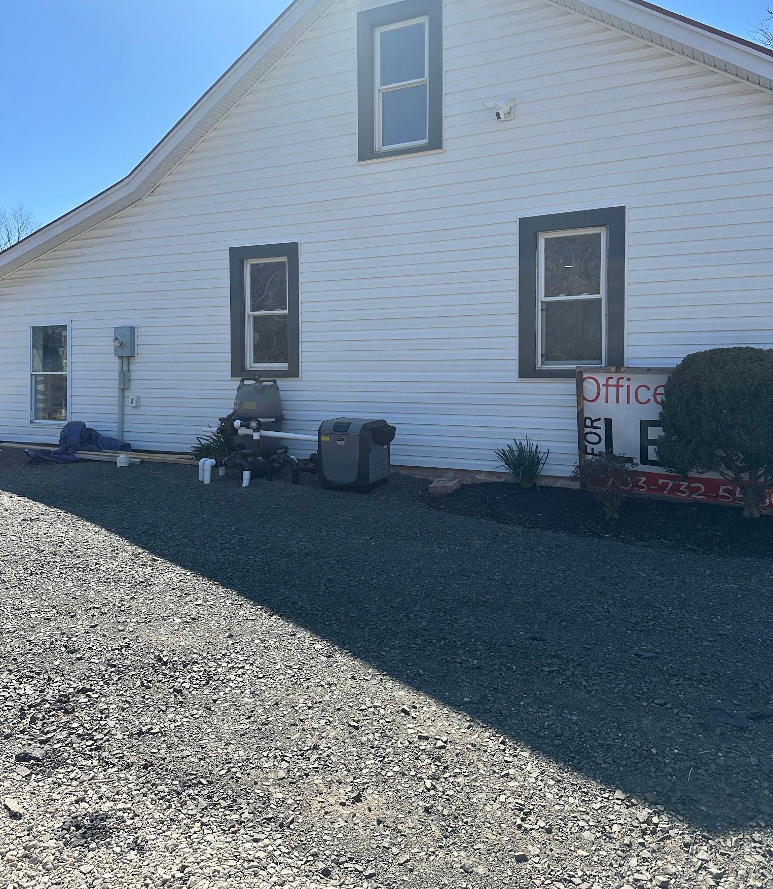 White building with several windows, dark trim, and a gravel driveway.