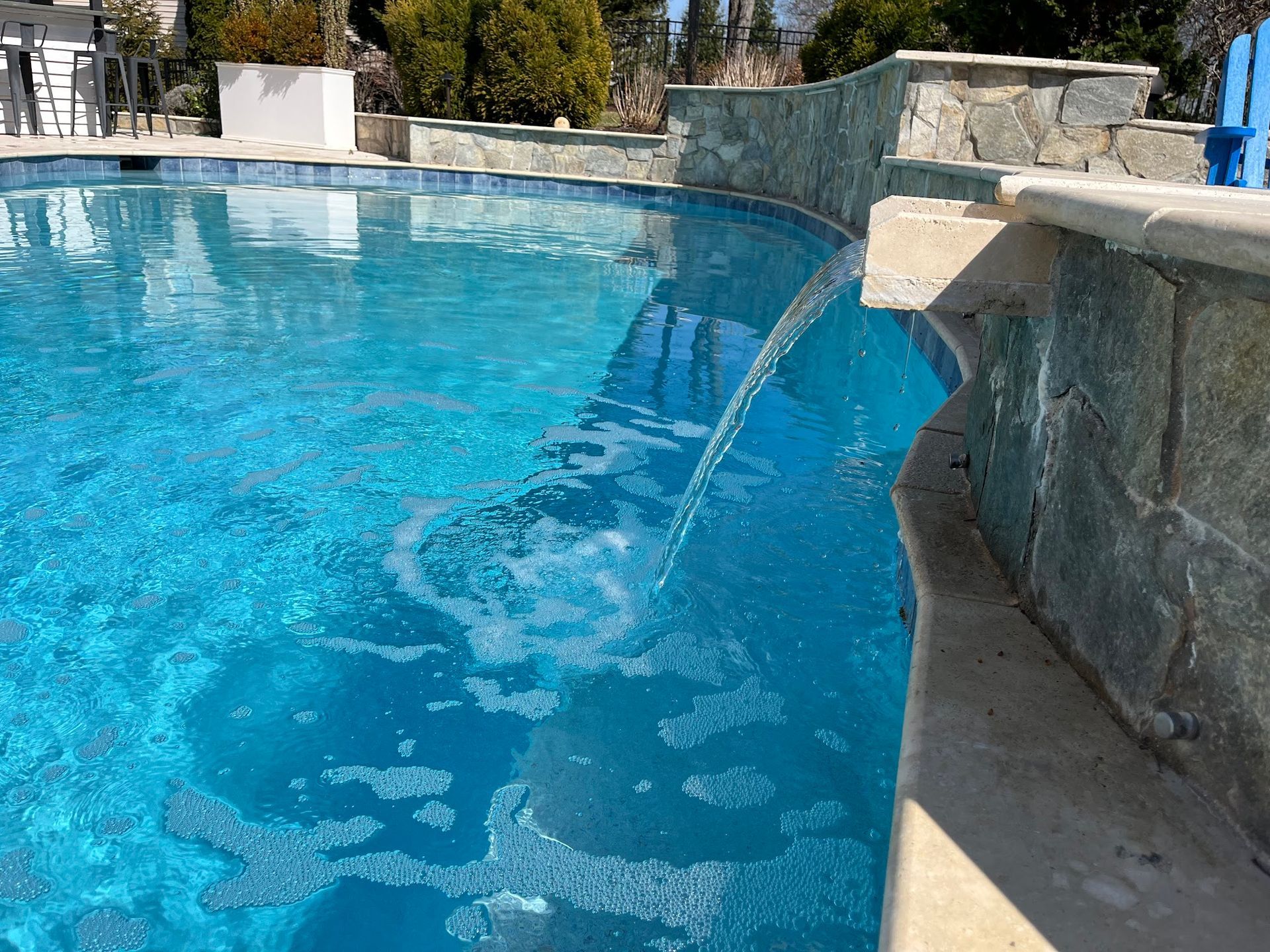 Blue pool with a waterfall feature, stone wall, and clear water cascading.