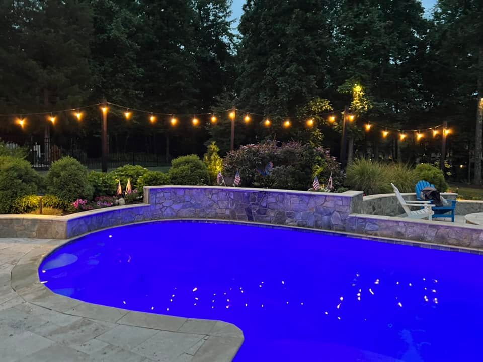 Pool lit with blue light, string lights overhead, outdoor setting.