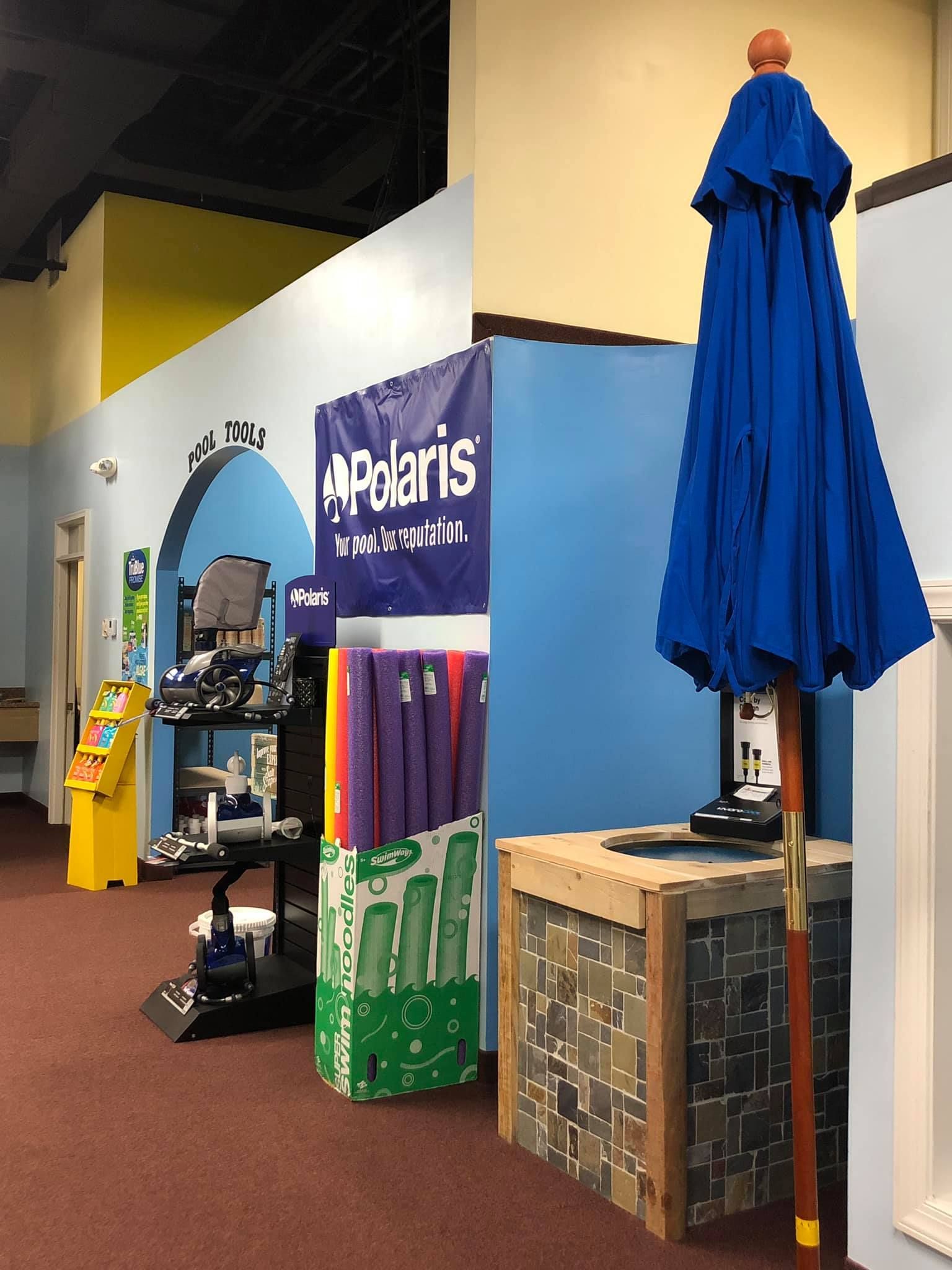 Blue umbrella standing next to a rustic wooden table with a blue wall in the background.