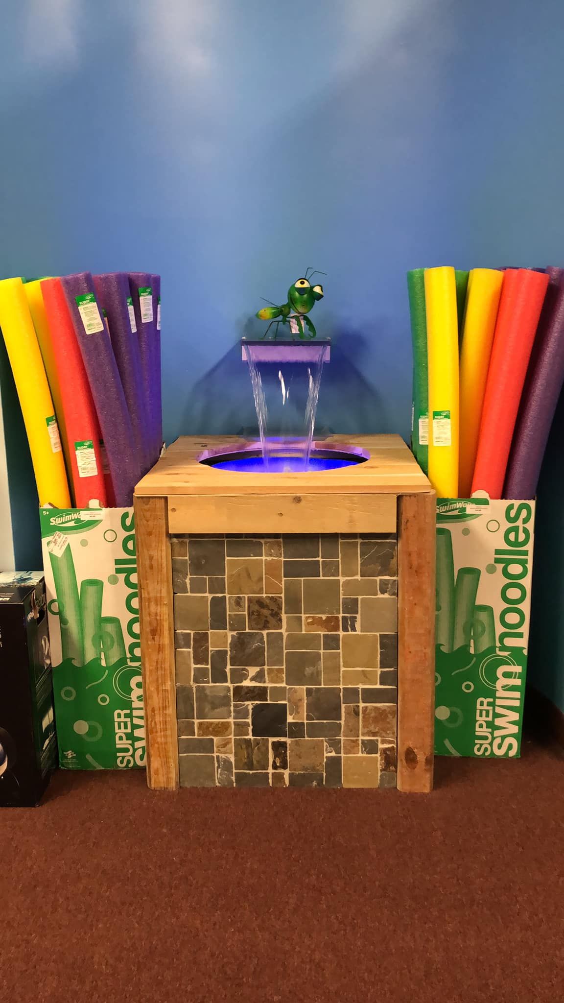 A fountain with a green dragon sculpture on a tiled cabinet, flanked by colorful swim noodles.