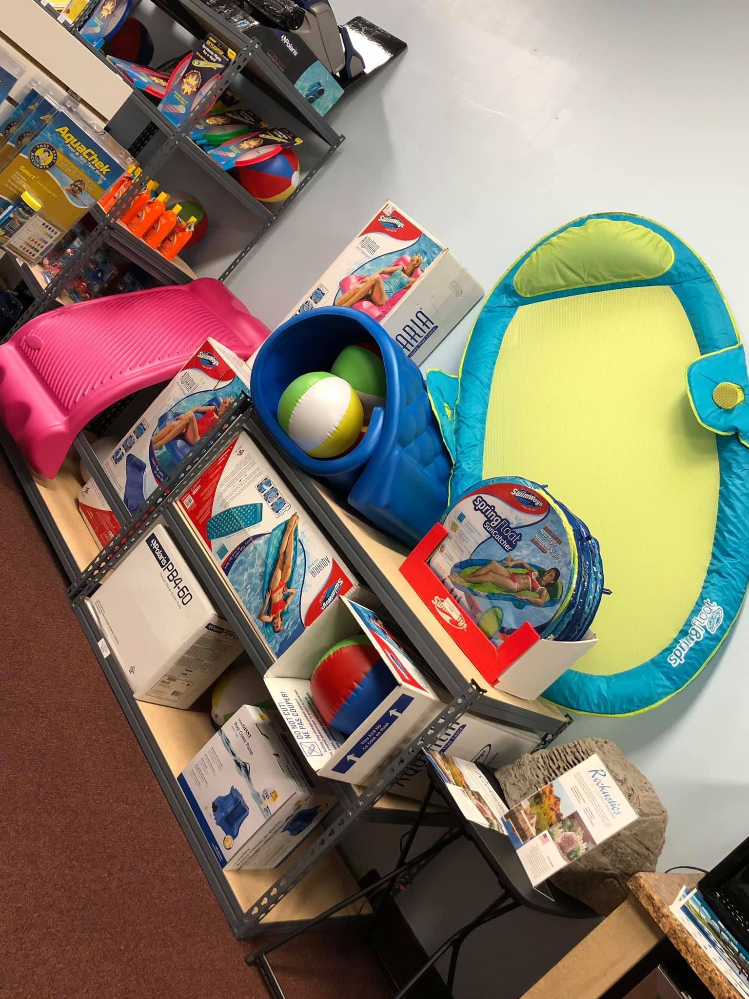 Beach toys displayed on shelves: inflatable floats, balls, paddles, and containers.