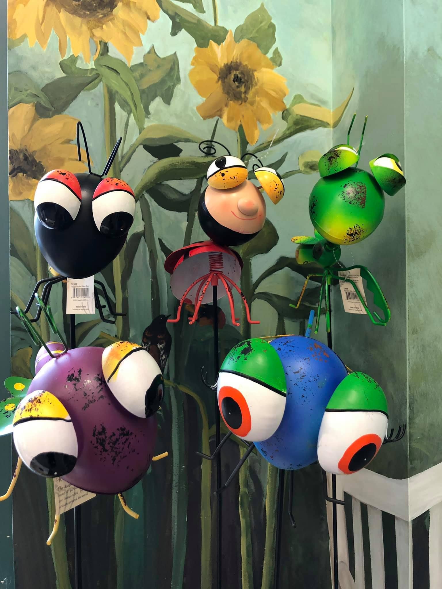 Metal bug yard art in various colors displayed against a sunflower mural.