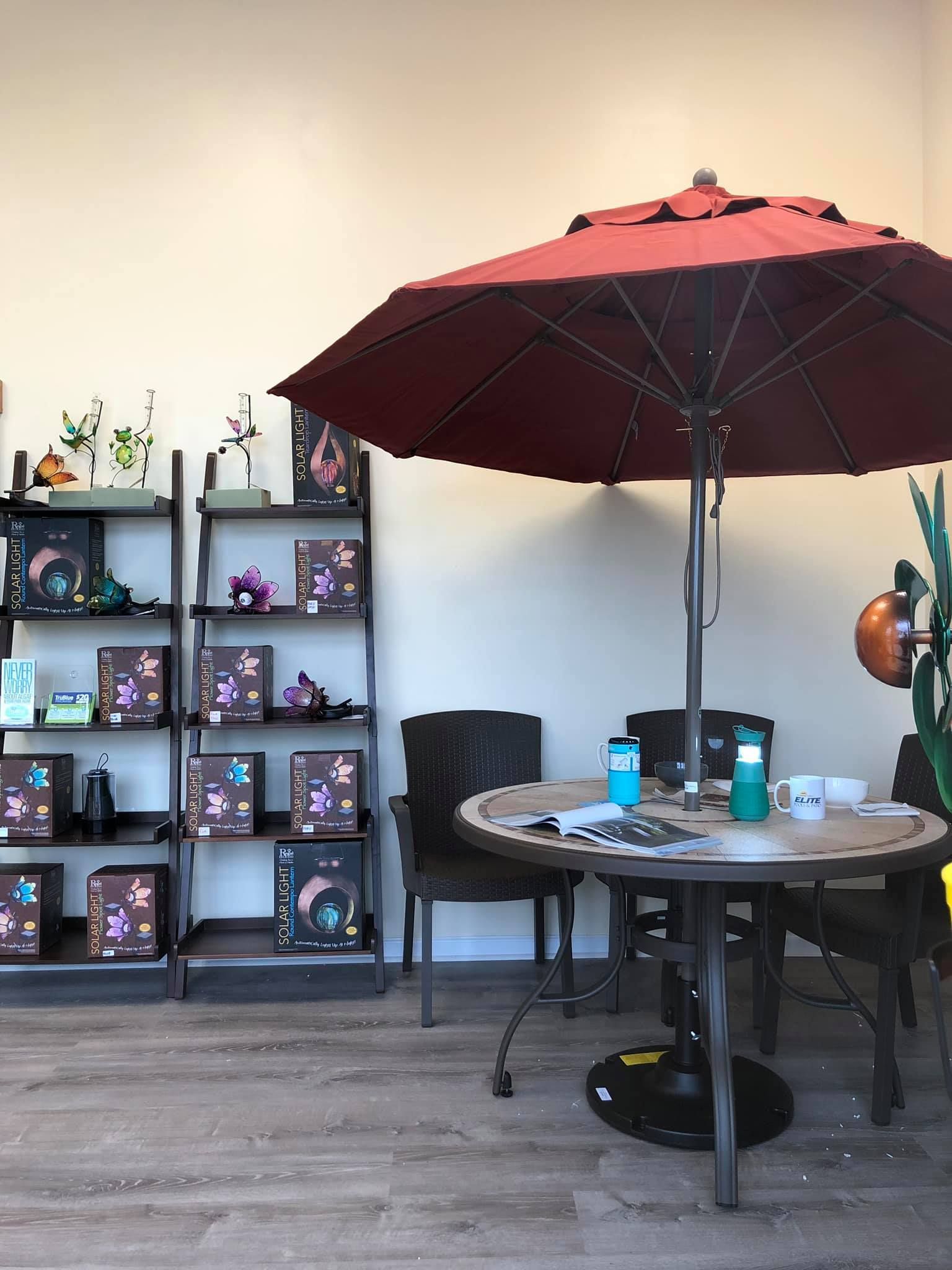 Shop interior with product shelves, round table, chairs, and a red patio umbrella.