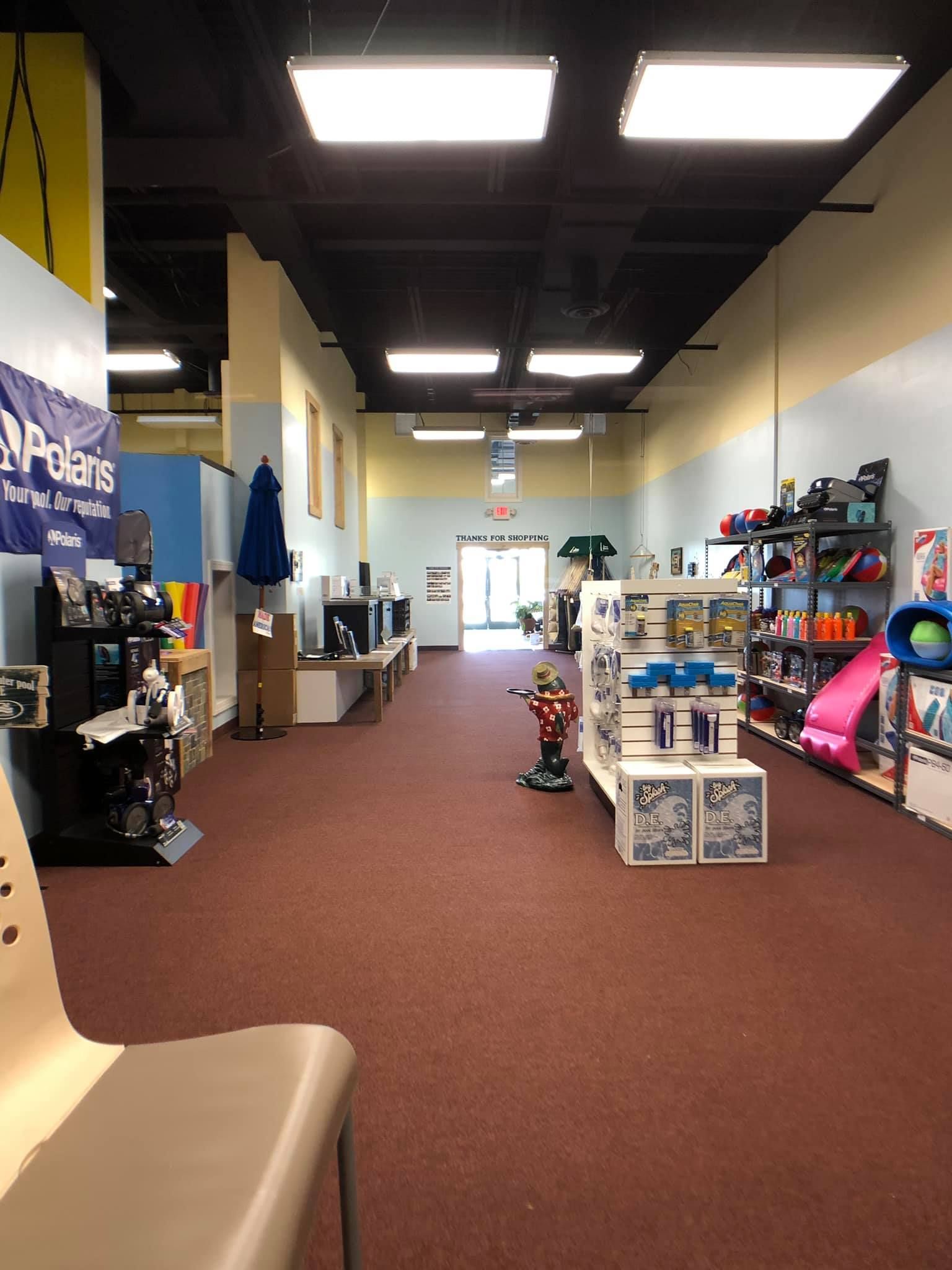 Interior of a retail store with merchandise displayed on shelves and in the middle of the floor. Reddish-brown carpet.