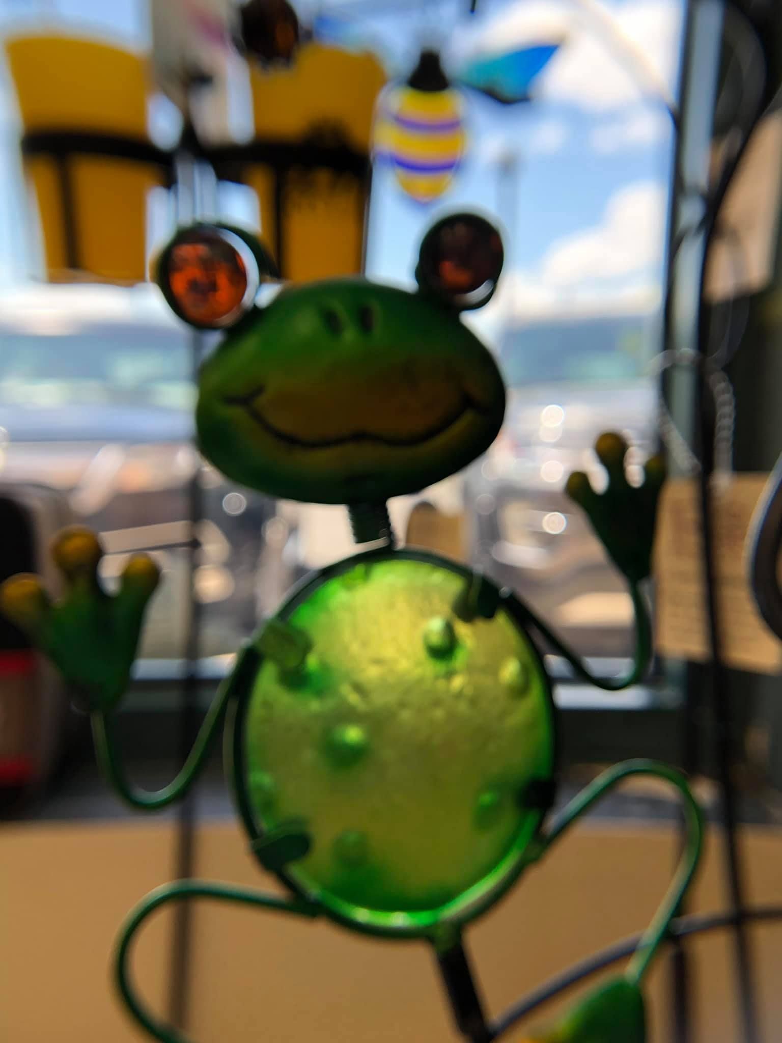 Green metal frog sculpture with big eyes and outstretched arms, smiling.