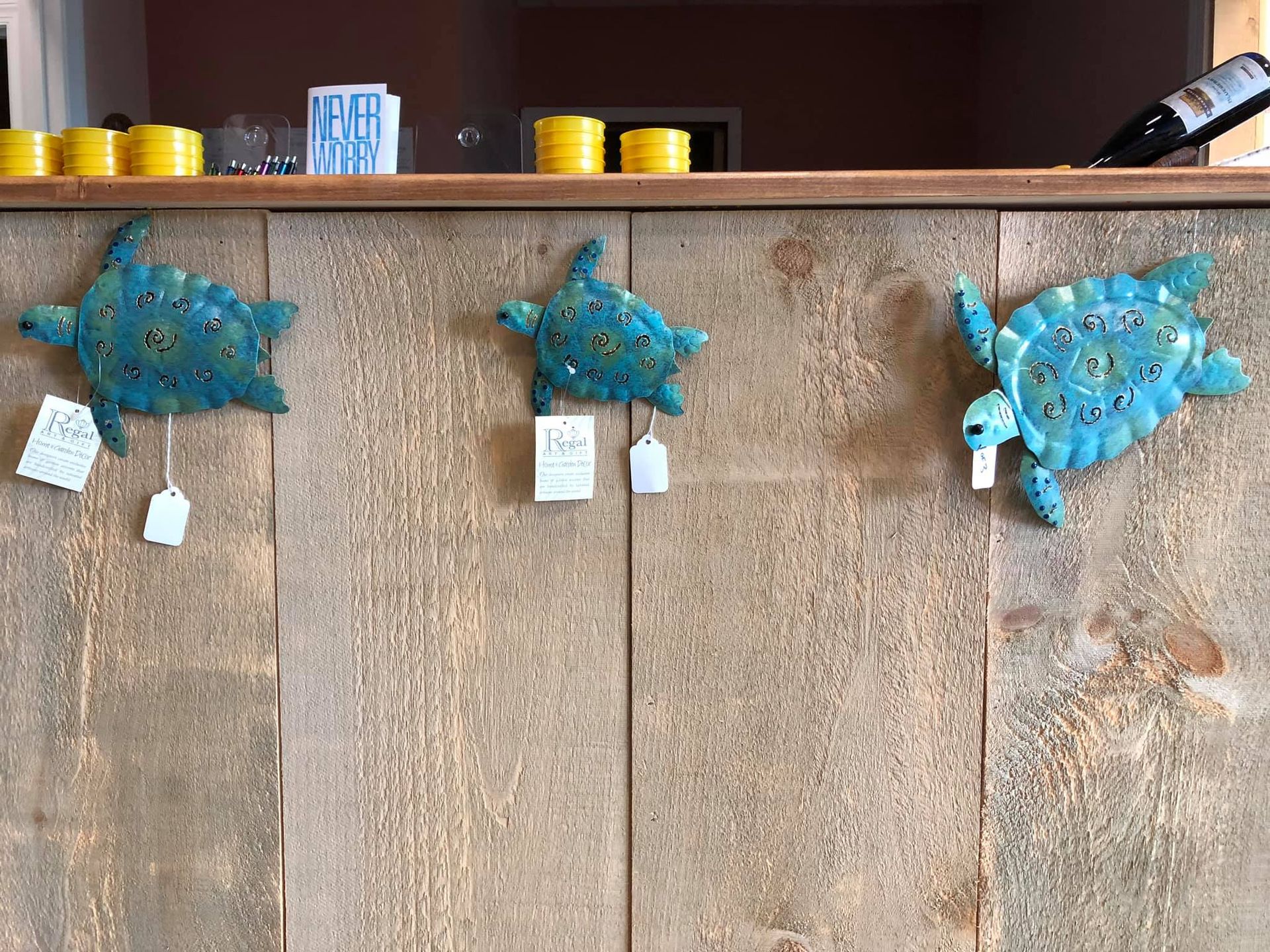 Three blue metal turtle decorations on a wood wall, with price tags hanging.
