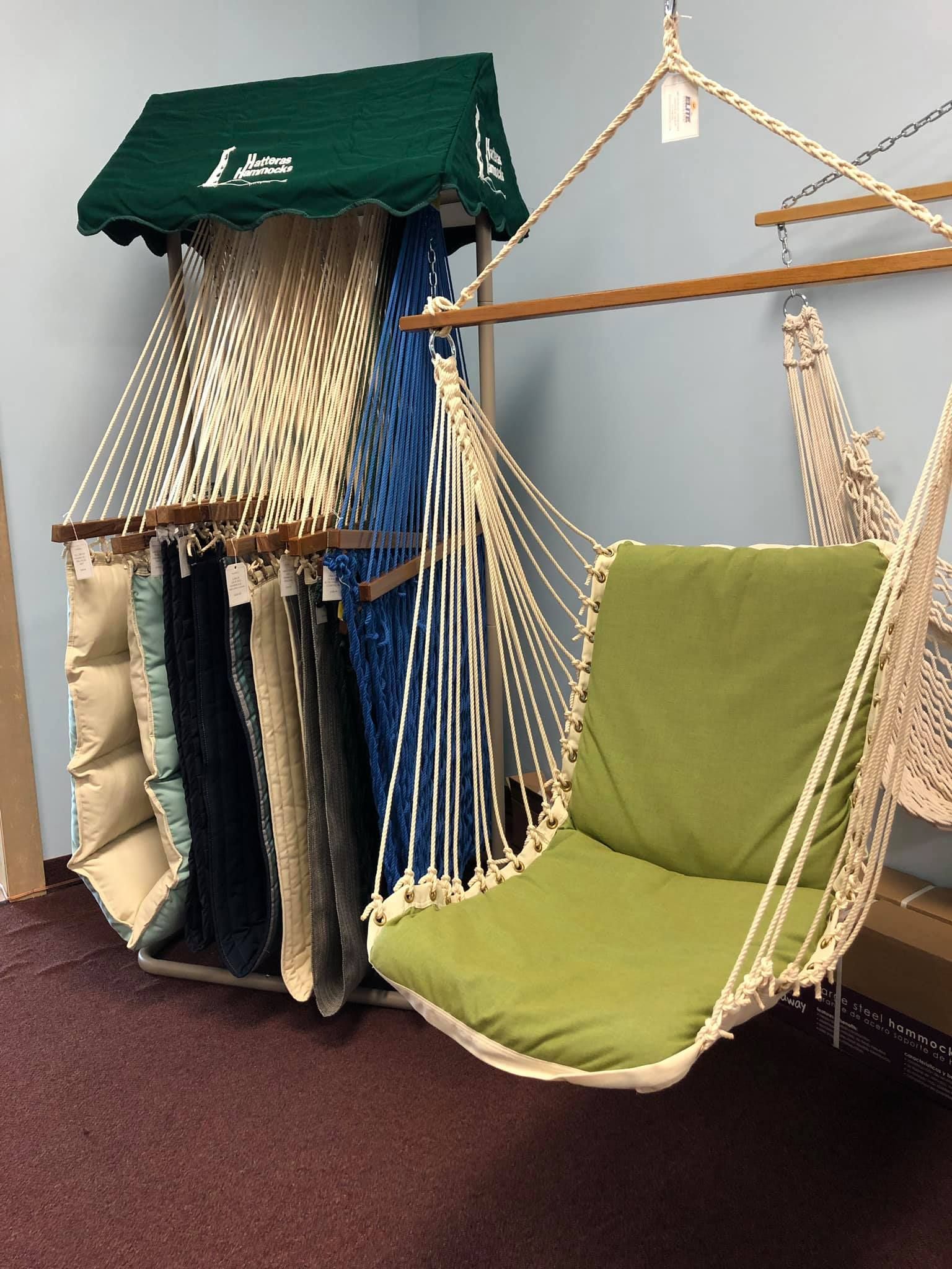 A hammock chair with a green cushion hangs next to a display of hammocks and fabric samples.