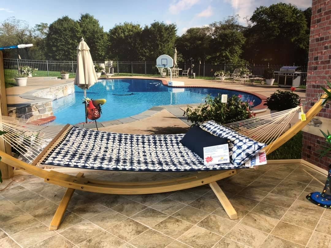 Hammock on patio, pool in background. Blue and white checkered hammock with a blue pillow.