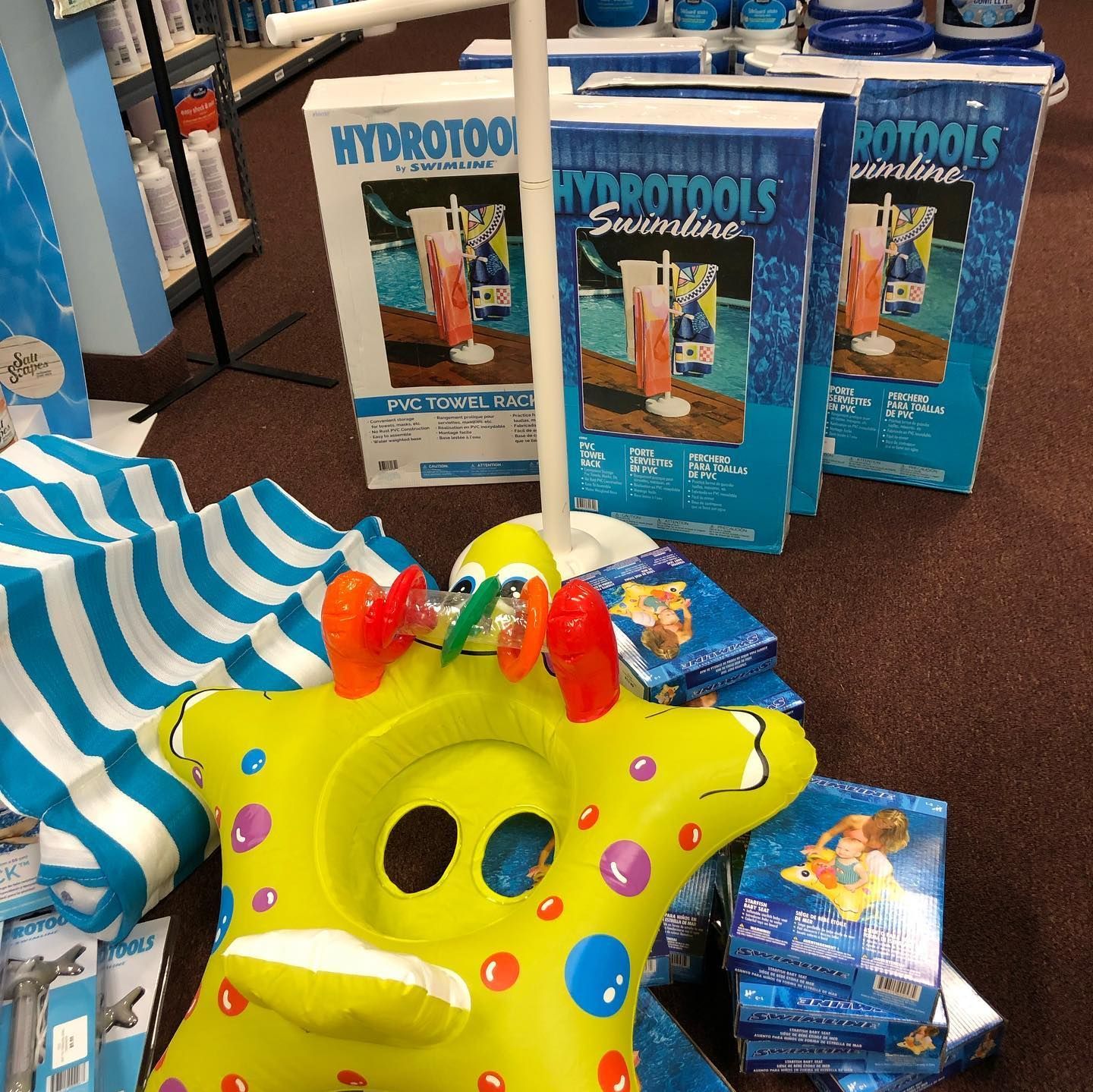 Pool supplies on display, including boxes of Hydrotools chemicals, a yellow inflatable starfish, & a striped beach umbrella.