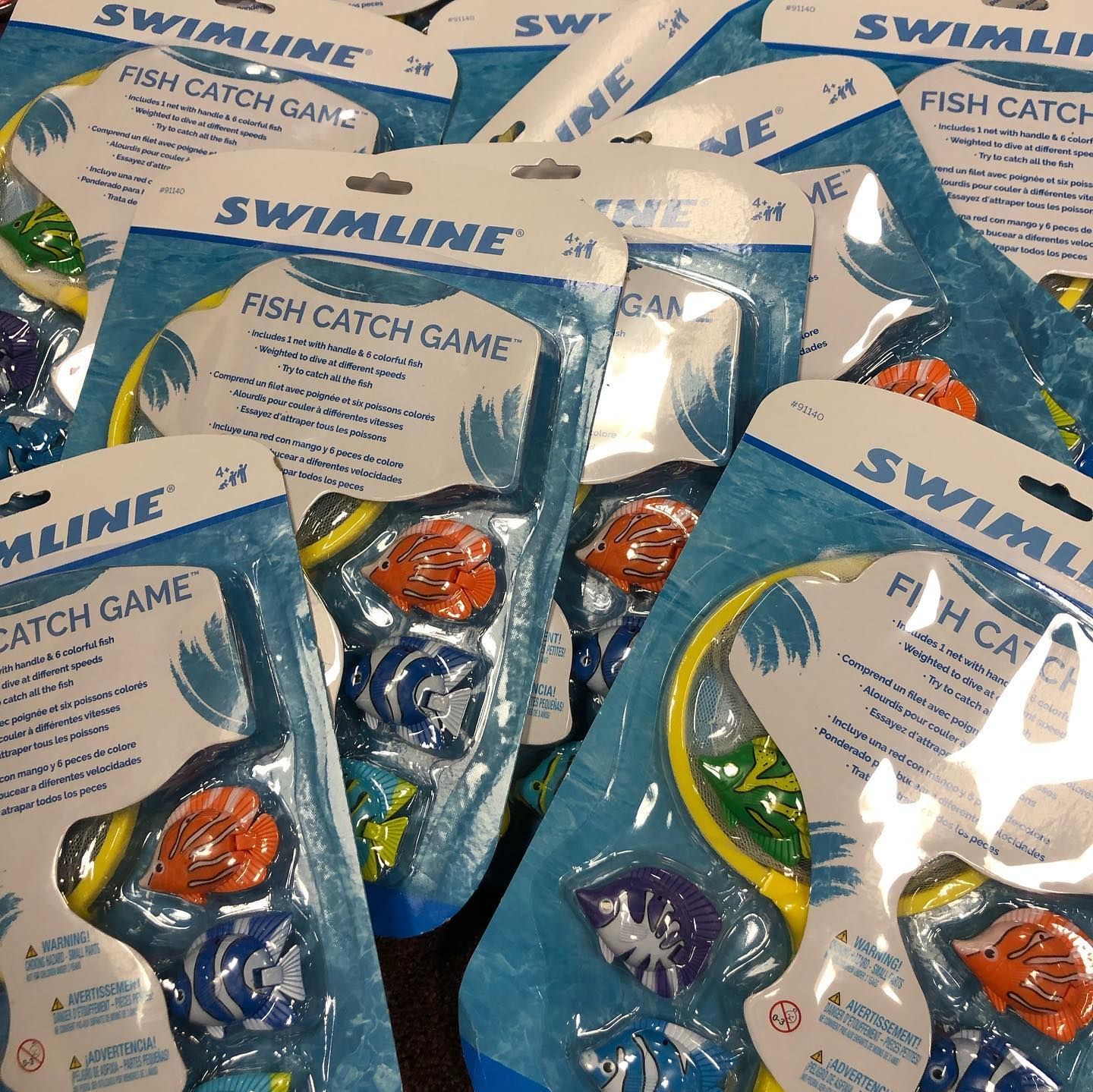 Pile of Swimline fish catch game packages, blue and white packaging with colorful fish toys.