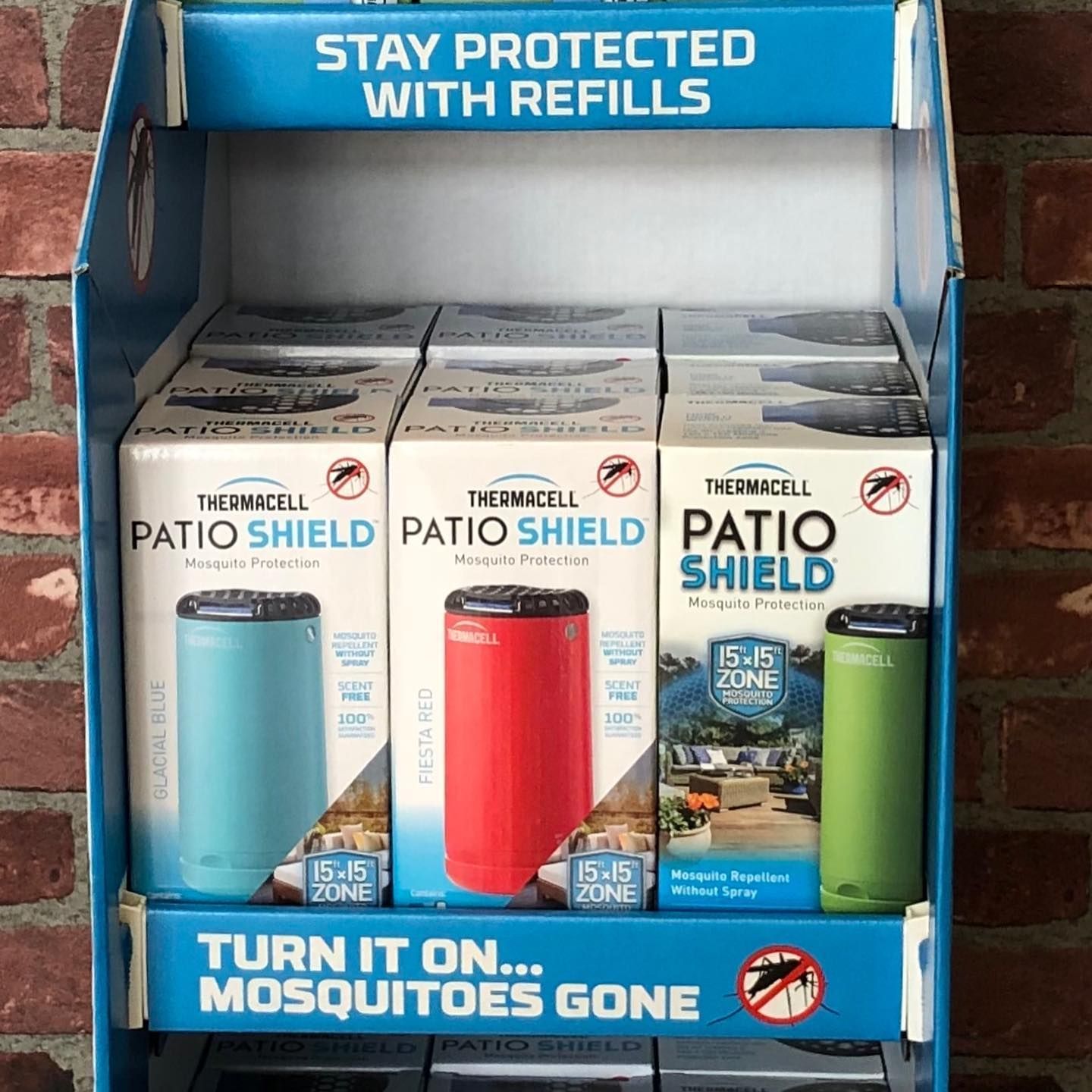 Display stand with three Thermacell Patio Shield mosquito repellent devices in blue, red, and green.