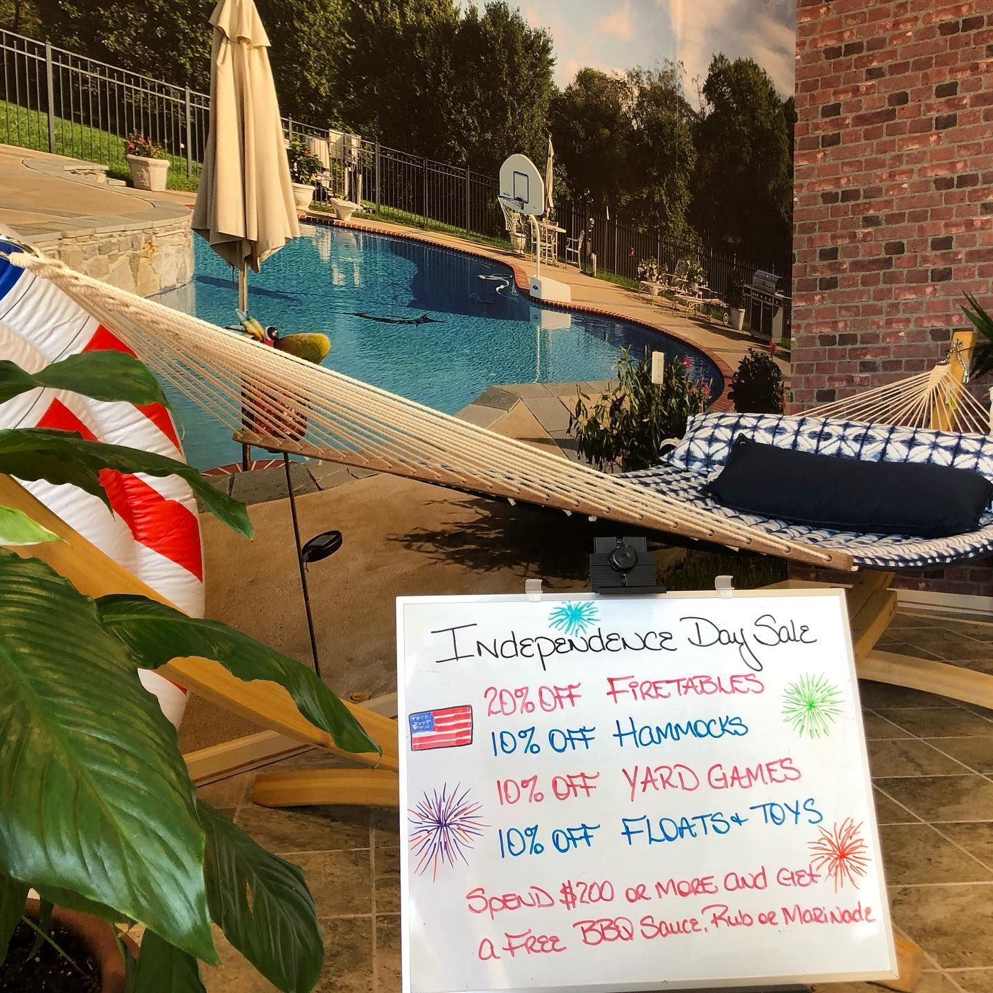 Sign advertising an Independence Day sale: 20% off firetables, 10% off hammocks, yard games, & floats/toys.