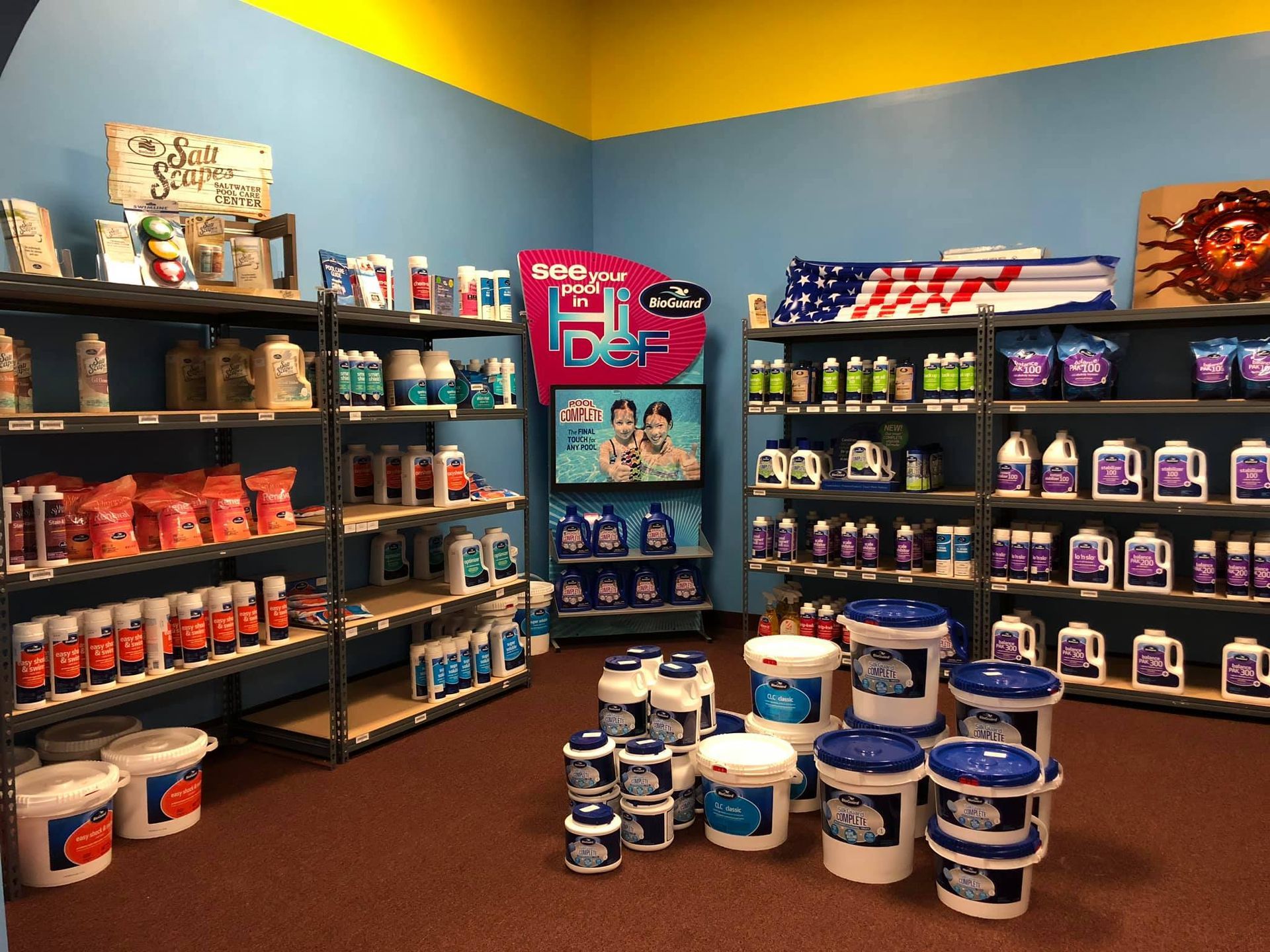 Shelves stocked with pool chemicals and supplies inside a retail store. Red, white, and blue products.