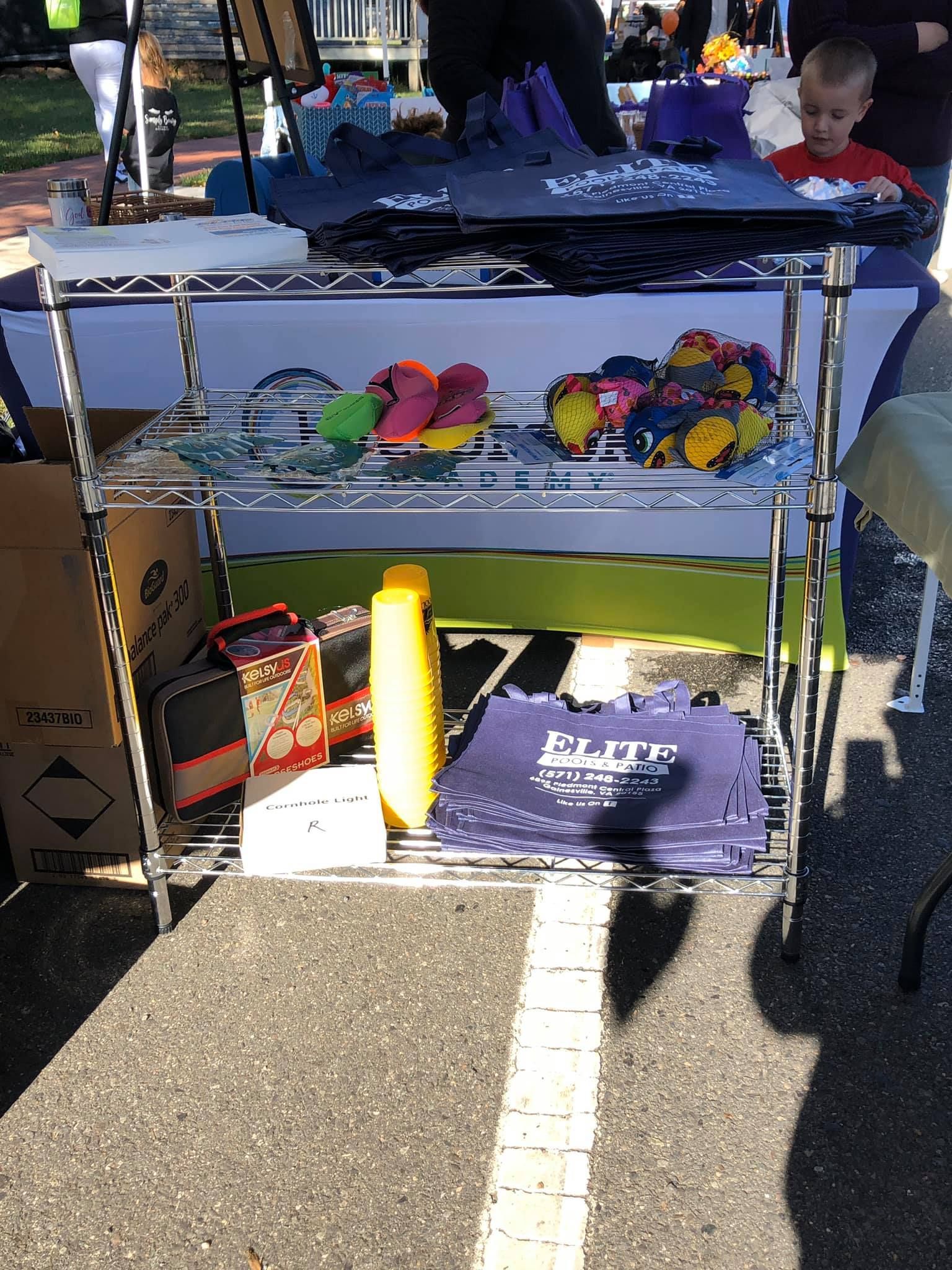 Metal shelving unit at an outdoor market with various items: plush toys, shirts, and a yellow bottle.